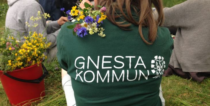 En rygg med grön t-shirt och Gnesta kommuns logga. Sommarblommor och grönt gräs i bakgrunden. 