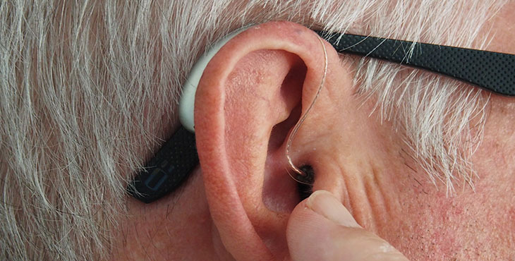 En äldre persons öra i profil med en hörselapparat. 