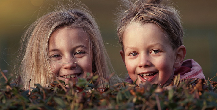 två glada barn, en pojke och en flicka, som gömmer sig bakom en buske