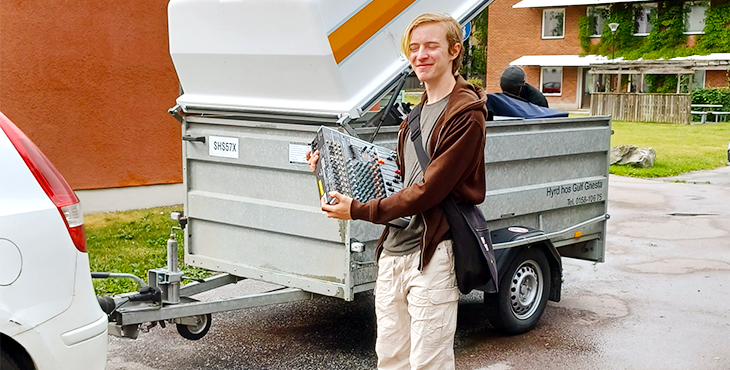 Nathan bär musikutrustning framför en släpkärra fylld av instrument.