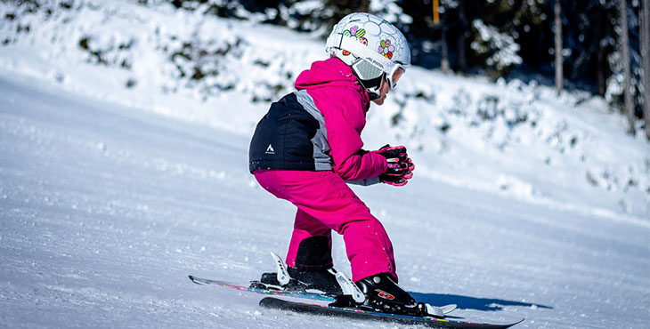 Ett barn i rosa overall och vit hjälm med blommor som åker nedför en slalombacke