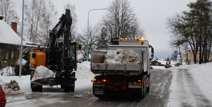 Bild på grävmaskin som lastar snö på flak på lastbil