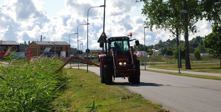 Traktor som klipper gräs i dike längs väg