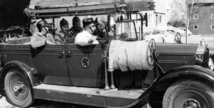 Fyra brandmän sitter i en gammal brandbil.