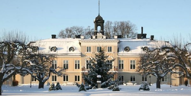 Herrgårdsliknande vitt slott med en snötäckt julgran i centrum. 